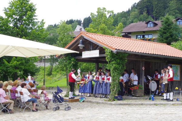 Im Kurpark von Sankt Englmar spielt eine Kapelle auf einem überdachten Veranstaltungsplatz. Besucher sitzen unter einem großen Baldachin und lauschen dem Konzert.
