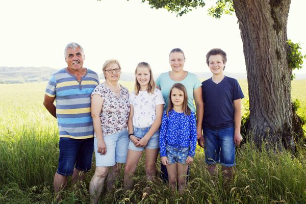 Eine Familie mit vier Kindern steht in einer Wiese unter einem Baum.