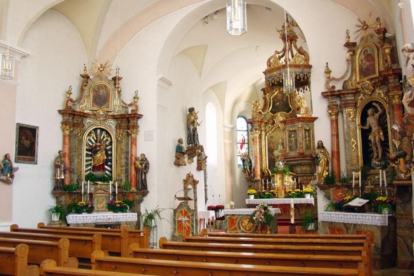 Kircheninnenraum mit Gewölbedecke, zentralem Hauptaltar, zwei Seitenaltären, Heiligenfiguren und Bankreihen.