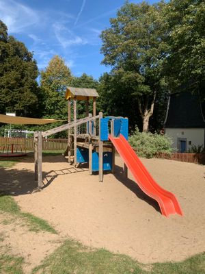 Das Bild zeigt einen Kletterturm mit Rutsche am Spielplatz in Lauenhain. Im Hintergrund sieht man ein Karussell.