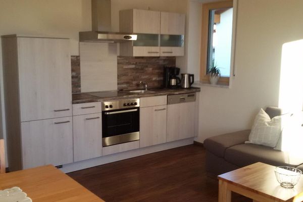 Die Wohnküche verfügt über einen Esstisch, Stühle sowie ein Sofa und davor ein kleiner Tisch. Ein Fenster direkt neben der hellen Küchenzeile spendet Tageslicht.