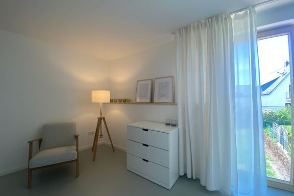 Auf dem Bild ist ein gemütlicher Sessel mit Stehlampe und großem Fenster zu sehen