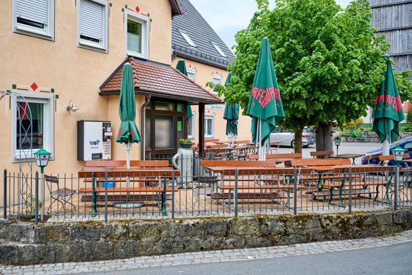 Blick auf eine Hausfassade und im Vordergrund einen Biergarten.