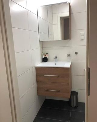 Ein Badezimmer mit einem Waschbecken und Unterschrank aus Holz, darüber hängt ein viereckiger Badspiegelschrank.